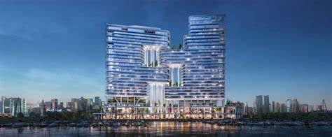 Modern curved high-rise towers with glowing facades along a waterfront at dusk, city skyline visible in the background