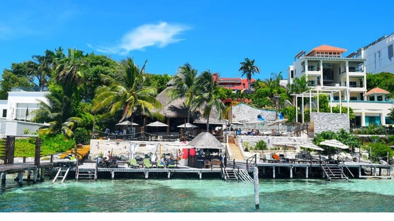Tropical waterfront resort with white buildings, palm trees, docks, and turquoise water under blue sky