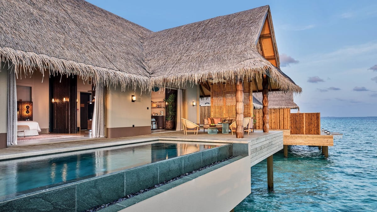 Luxury overwater bungalow with thatched roof, infinity pool, and wooden deck overlooking turquoise ocean.