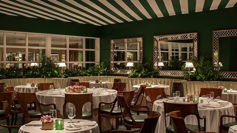 Elegant dining room with green walls, white tablecloths, wooden chairs, and decorative floral arrangements