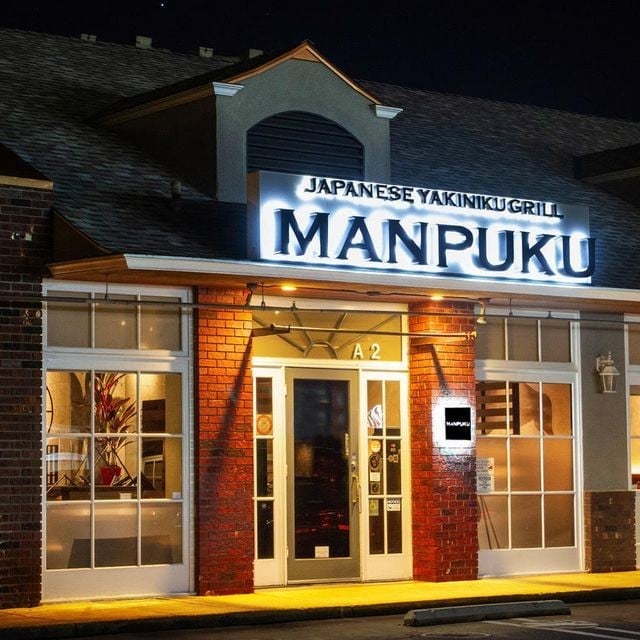 Japanese Yakimiku grill restaurant Manpuku with illuminated storefront, brick facade, and glass doors at night