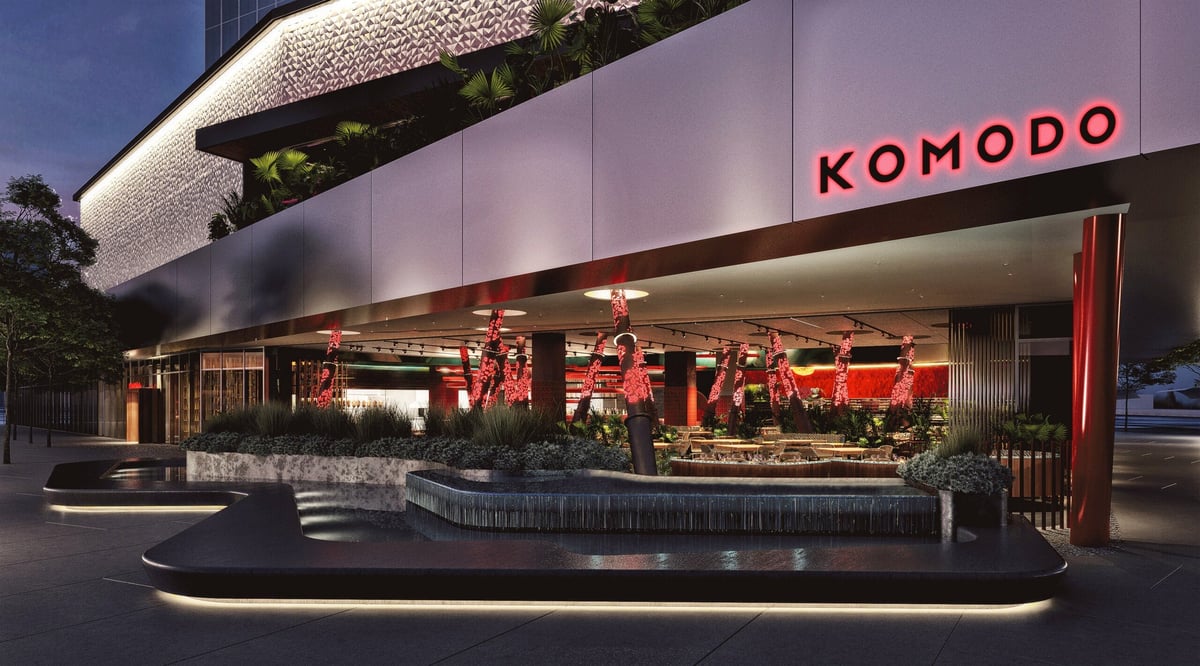 Modern Komodo restaurant exterior at night with illuminated signage, curved white architectural elements, and landscaped entrance
