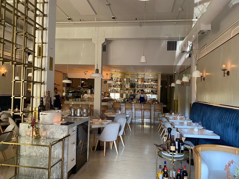 Modern restaurant interior with bar counter, dining tables, blue chairs, and upholstered banquette seating in an open industrial-style space