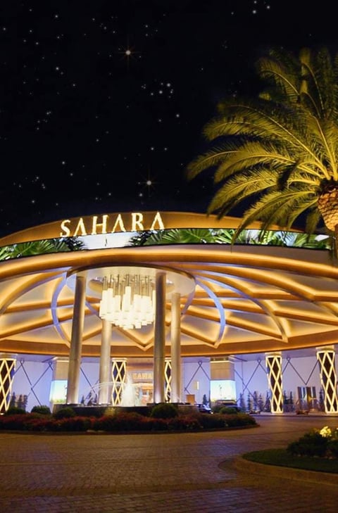 Nighttime exterior of illuminated Sahara hotel casino with palm tree and starry sky backdrop