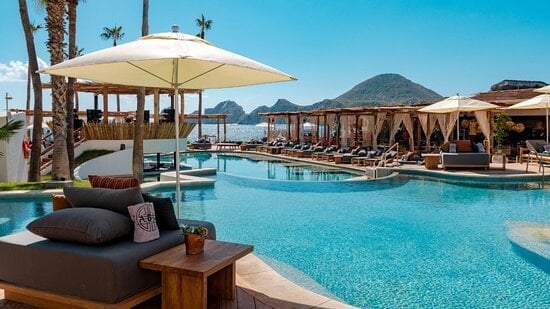 Luxury resort pool with blue water, lounge chairs, beige umbrellas, and mountain views in background
