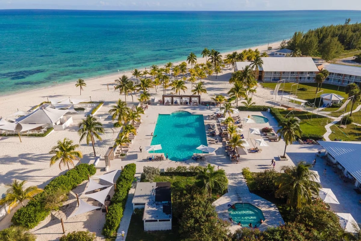 Aerial view of a luxury tropical beach resort with turquoise pools, white sandy beach, palm trees, and ocean waterfront