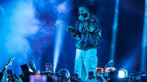 Rapper performing on stage under blue lighting with audience holding up phones