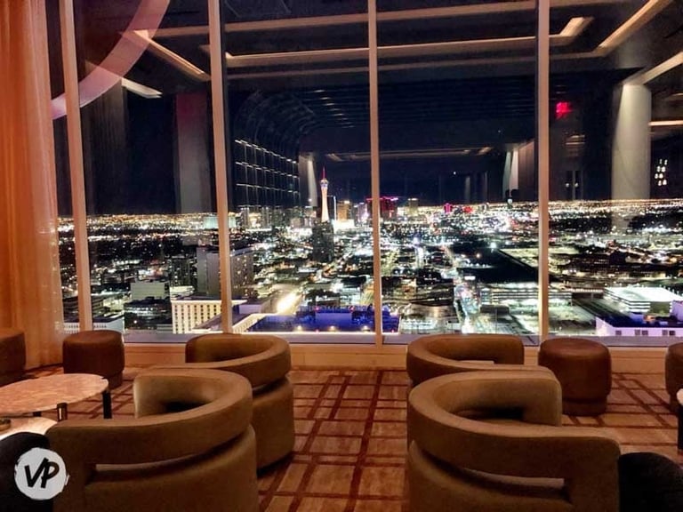 Modern lounge with curved tan seating overlooking a sprawling night cityscape through floor-to-ceiling windows