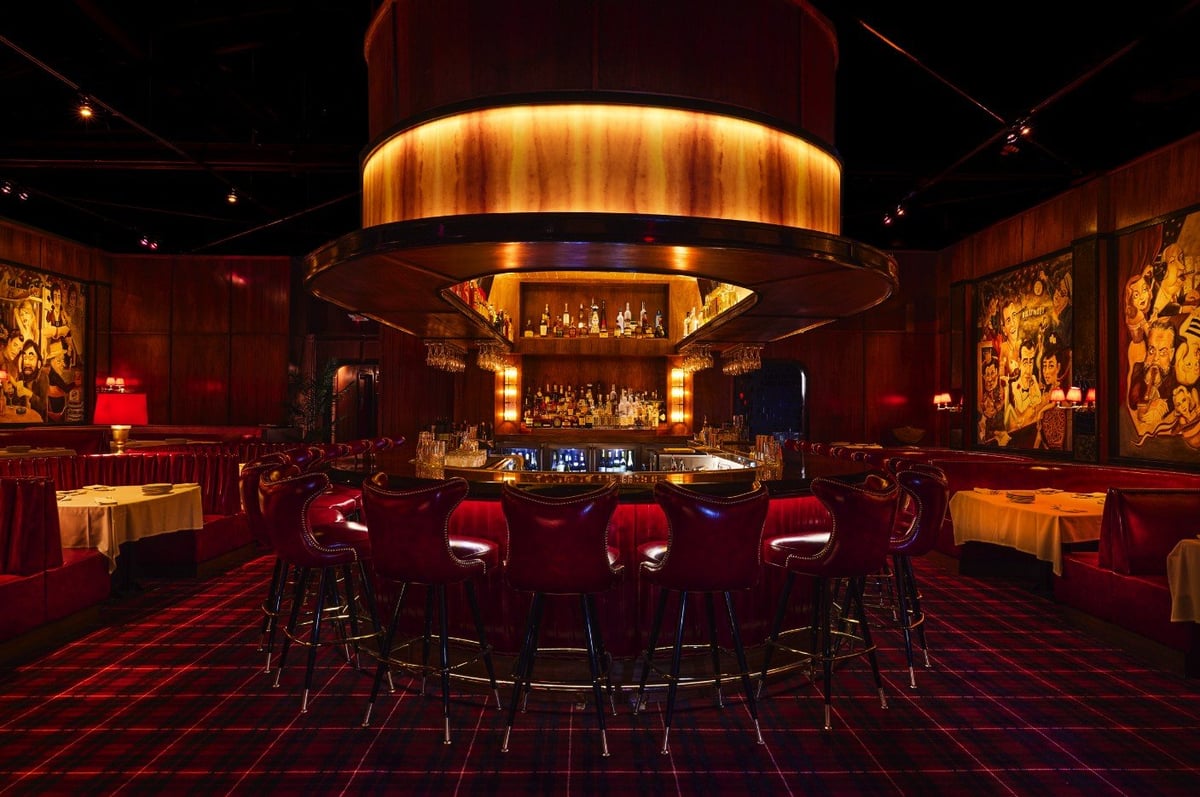 Upscale hotel bar with circular illuminated ceiling, red leather seating, and golden artwork on burgundy walls