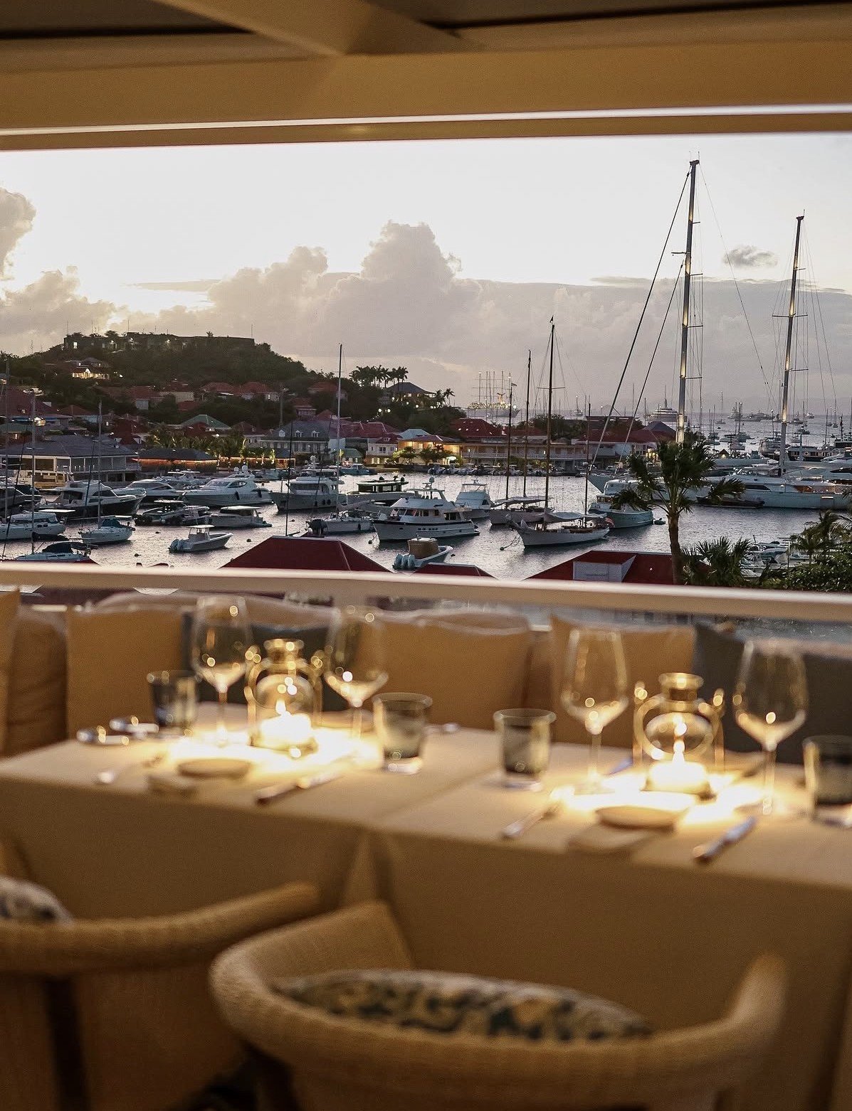 Upscale waterfront restaurant dining room overlooking a marina filled with sailboats at sunset