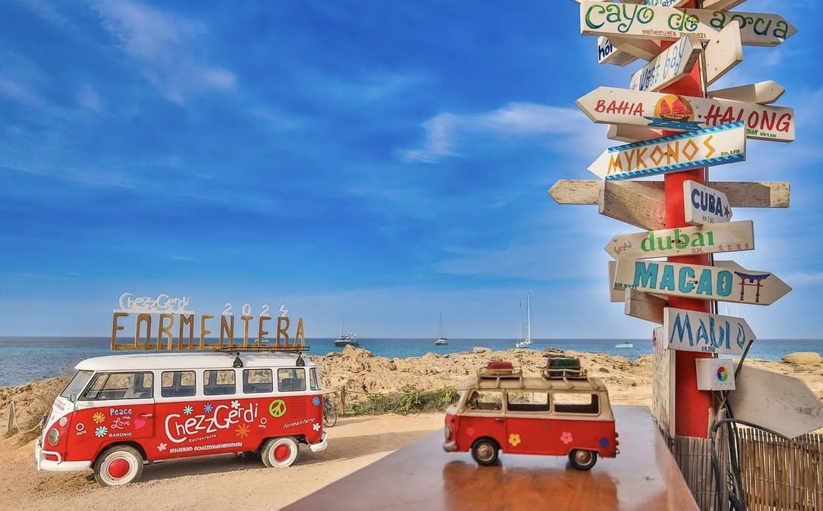 Red vintage van and truck at Formentera sign with directional wooden signs under blue sky