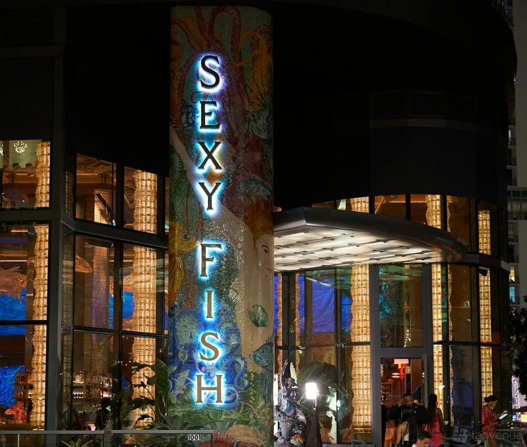 Neon Sexy Fish sign illuminated at night on a brick building with surrounding storefronts