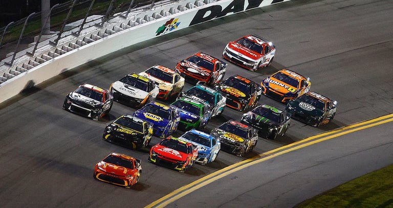 NASCAR stock cars racing in formation on a banked track with yellow line markings and white guardrails
