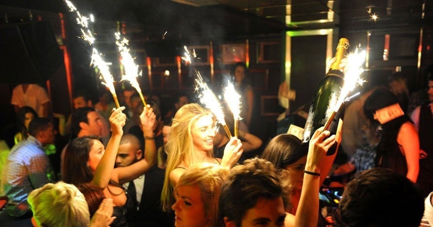 Group of people at a nightclub holding up sparklers and cold sparkler fountains during a celebration