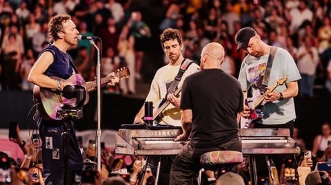Band performing on stage with lead singer at microphone, guitarist, keyboardist, and drummer