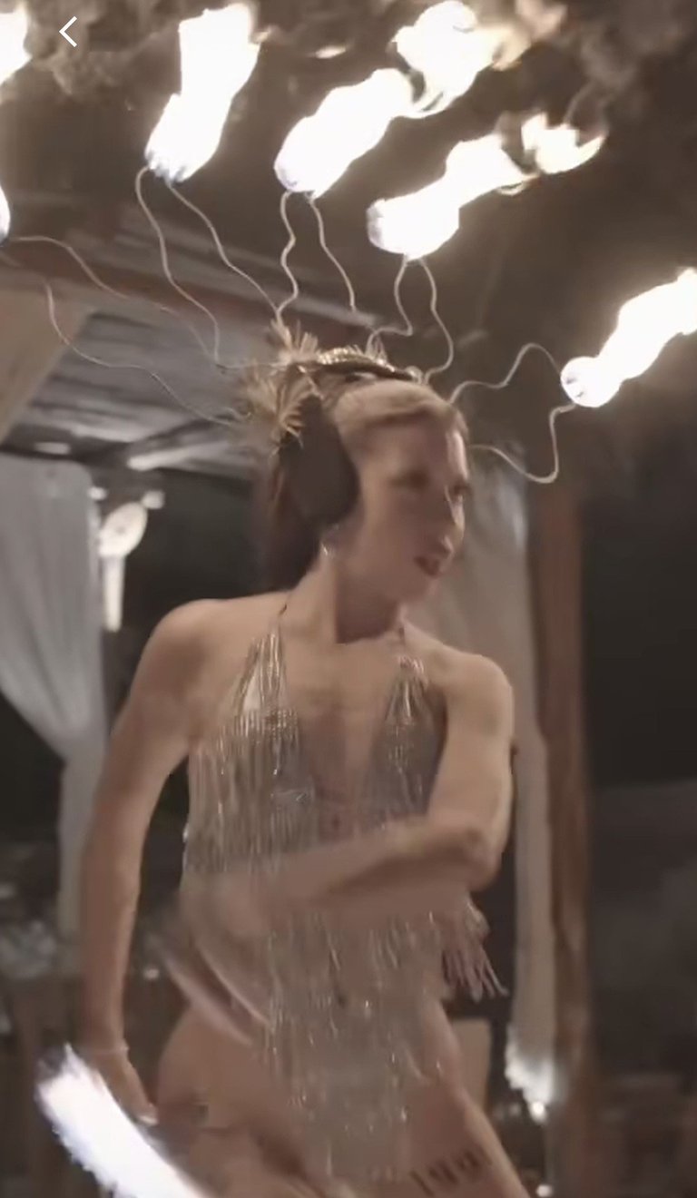 Woman in beige fringed dress posing under artistic light fixtures with wavy white glowing elements overhead