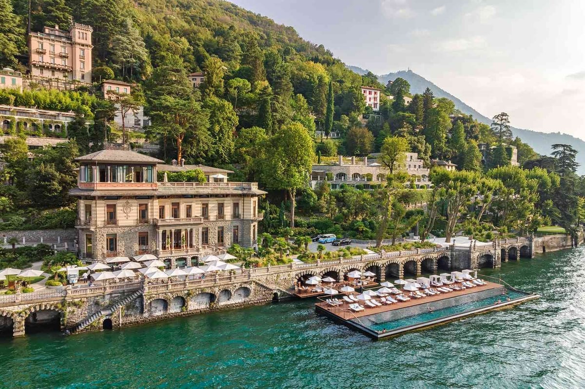 Elegant villa on turquoise lake waterfront with forested hillside and terrace boats, Alpine lakeside architecture
