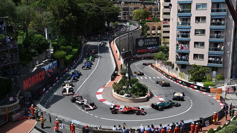 Formula 1 race cars navigating a tight corner on the Monaco Grand Prix street circuit with buildings and spectators visible