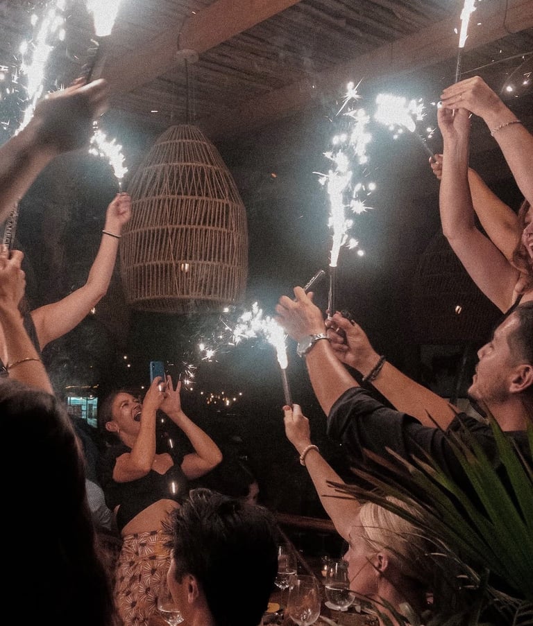 Crowd holding sparklers at night celebrating indoors with decorative birdcage and festive lighting overhead