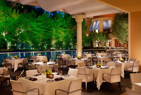 Elegant banquet hall with round tables set for dinner, modern chairs, outdoor garden views with green ivy walls and ambient lighting.