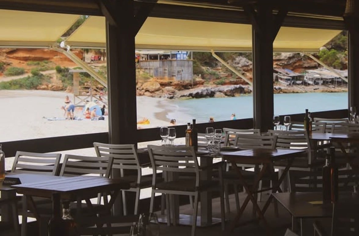 Restaurant interior with dark wooden tables and chairs overlooking a beach through large windows