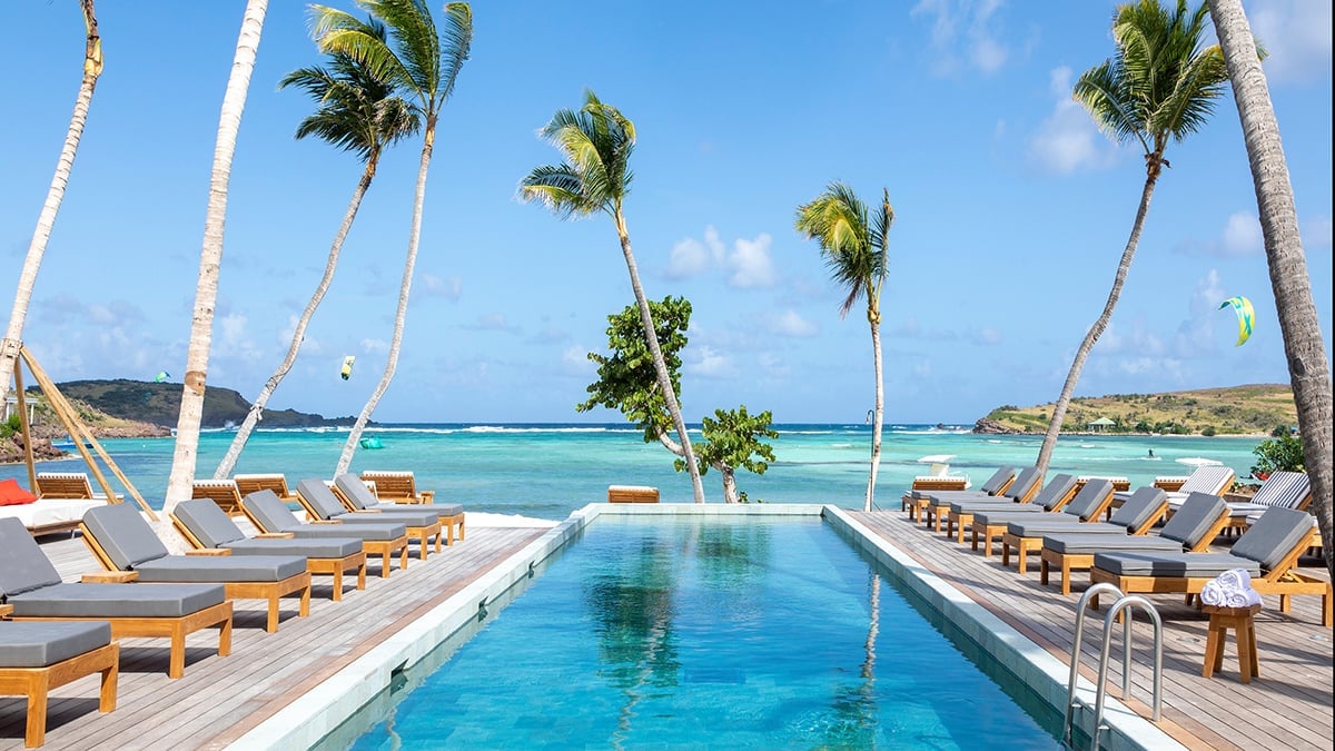 Luxury resort infinity pool lined with lounge chairs and palm trees overlooking turquoise ocean