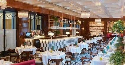 Elegant fine dining restaurant interior with white tablecloths, blue-striped bar, wooden paneling, and warm lighting
