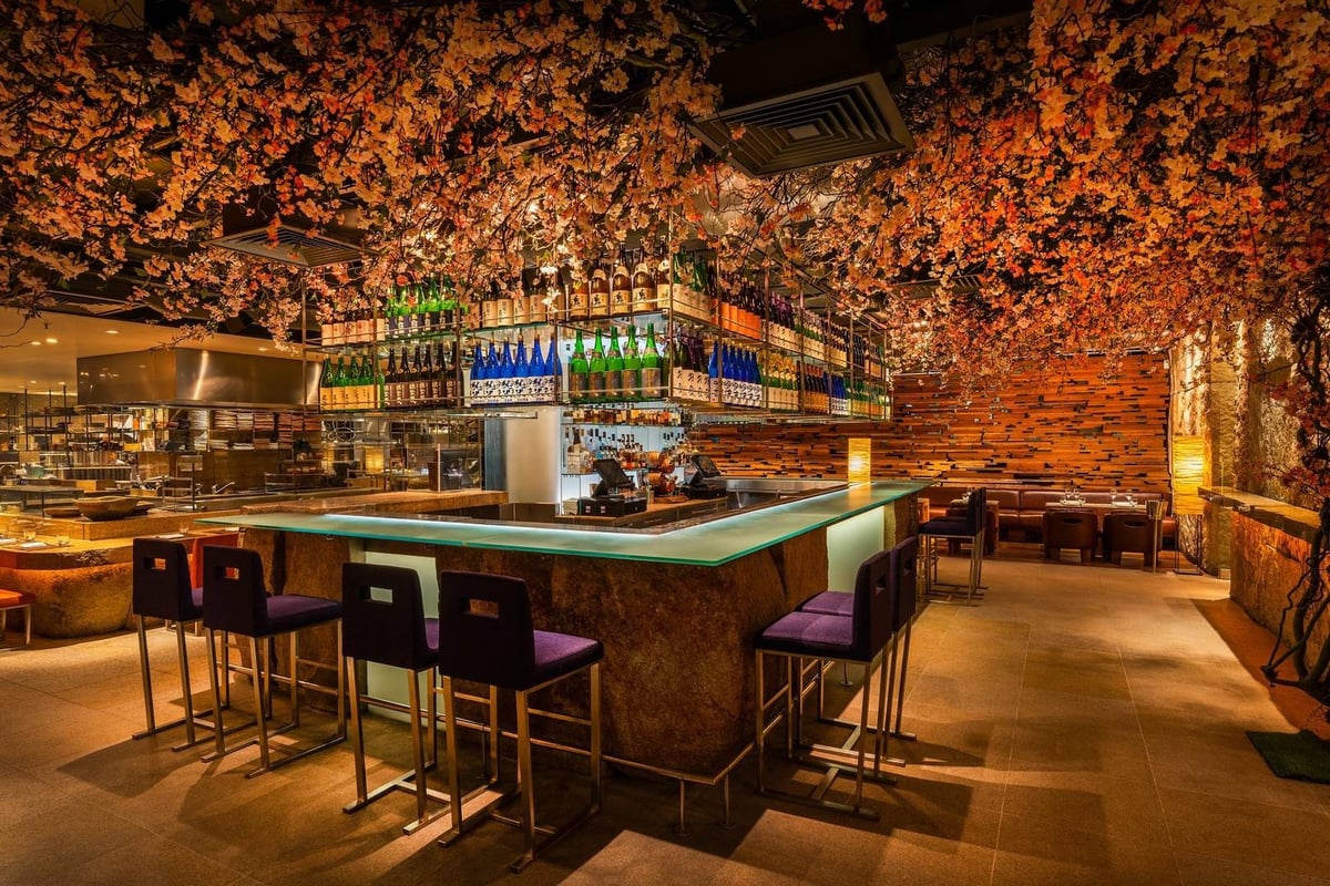 Modern bar interior with illuminated brick ceiling, counter seating with purple stools, and stocked shelves of bottles