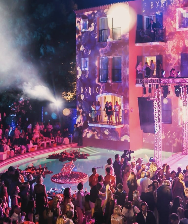 Nightclub event with crowd dancing on floor, illuminated pink and purple building facade with pyrotechnics and stage lighting