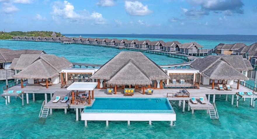 Aerial view of overwater bungalows and villas in turquoise lagoon with thatched roofs and wooden pathways at tropical resort