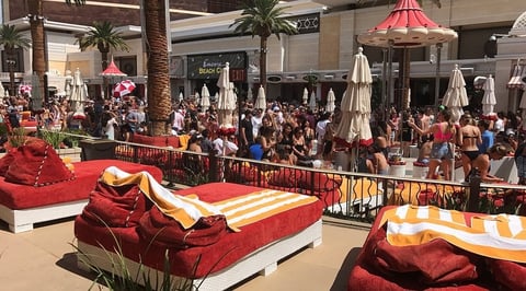 Busy outdoor courtyard with large red and gold decorative installations, umbrellas, and crowds of people walking around.