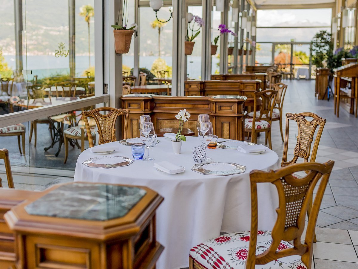 Elegant restaurant dining room with round table set with white tablecloth, place settings, and wooden chairs overlooking large windows with ocean view