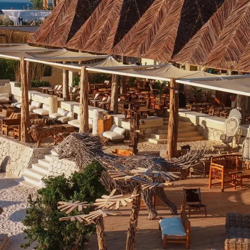 Luxury beach club with wooden pergolas, lounge seating, and thatched roof structures overlooking the sea