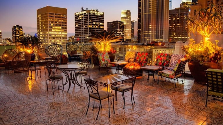 Rooftop patio with dining tables, colorful lighting, and city skyline at dusk