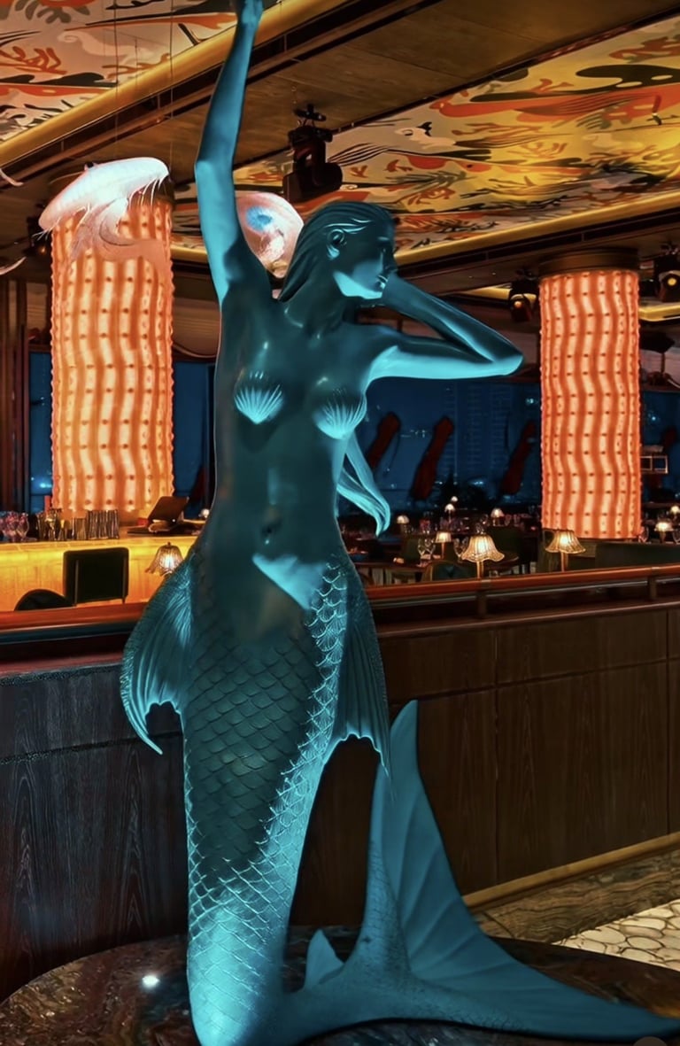 Glowing blue mermaid statue with arm raised inside a casino lounge with decorative orange pillars and bar