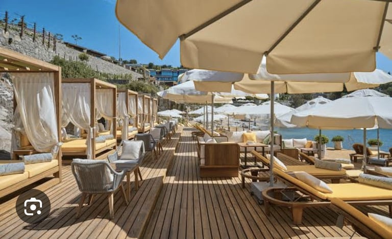 Luxury beach club with beige umbrellas, wooden loungers, and cabanas overlooking the Mediterranean Sea under clear blue sky