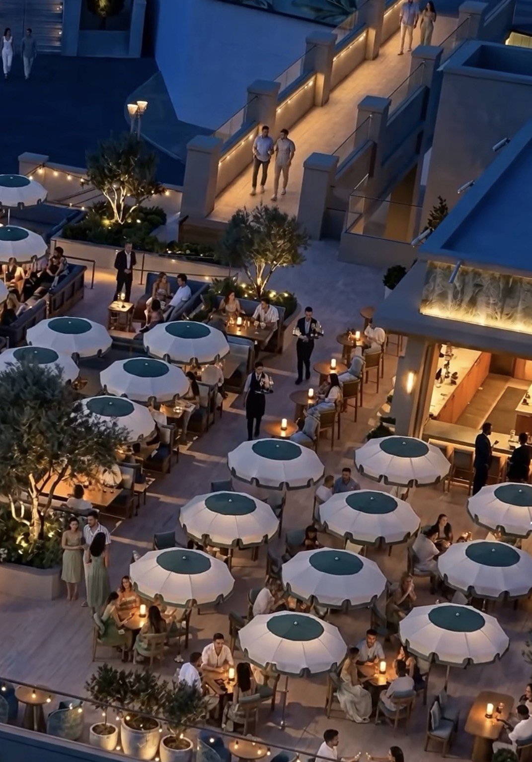 Aerial view of an upscale rooftop event with white umbrellas, guests dining and socializing at tables, warm lighting at dusk