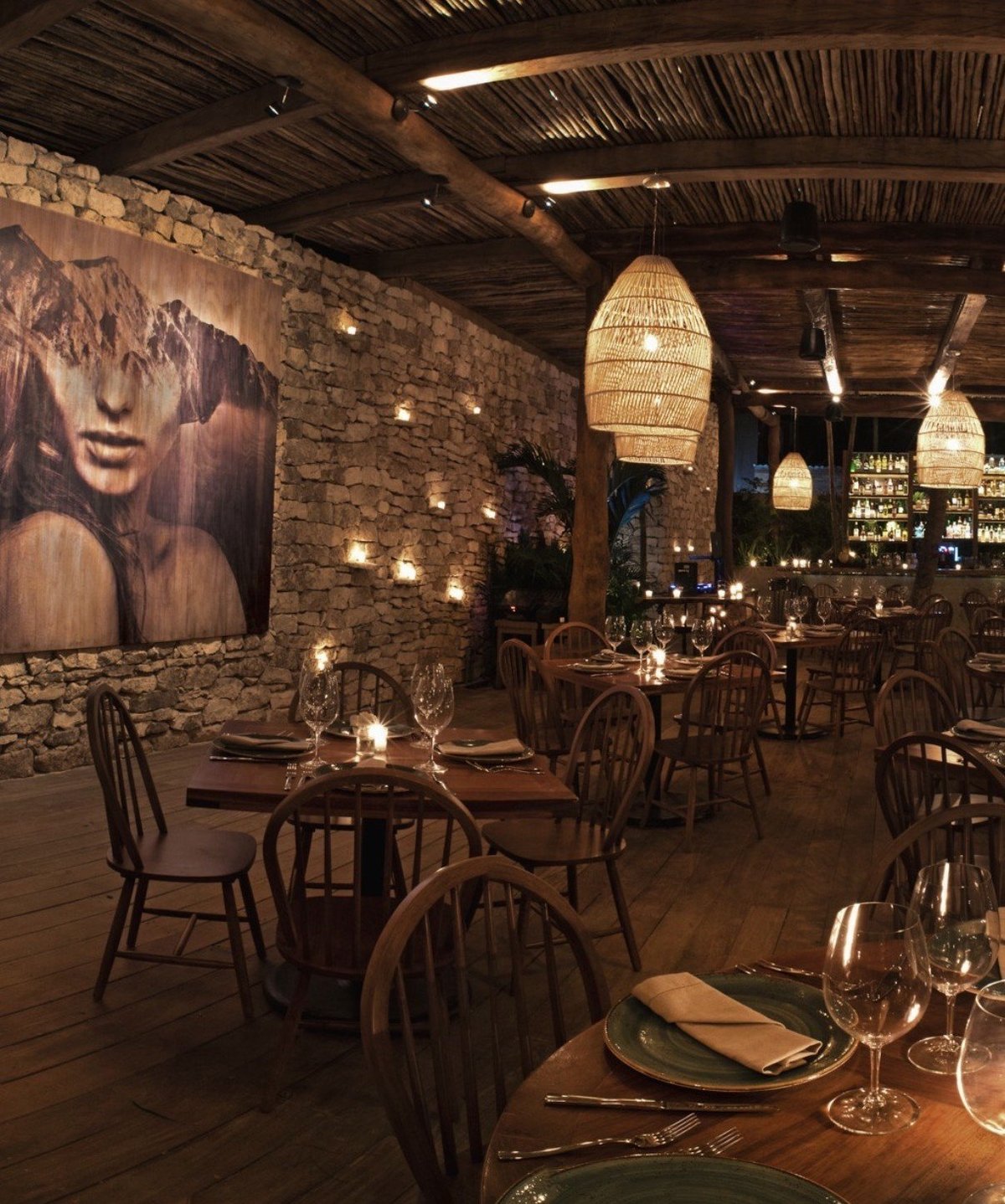Upscale restaurant interior with exposed brick walls, wooden chairs, warm pendant lighting, and table settings with glasses and place cards.