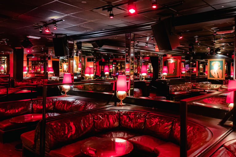 Red-lit nightclub interior with plush seating, neon lighting, and intimate booth areas