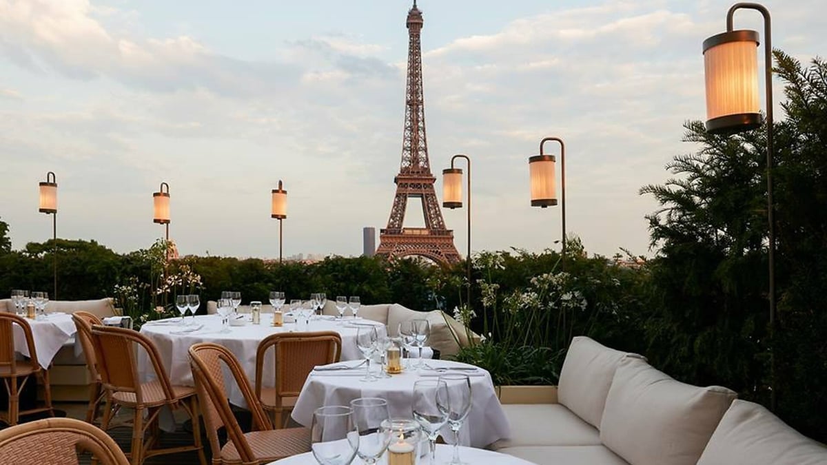 Elegant outdoor dining terrace with white tablecloths overlooking the Eiffel Tower in Paris at sunset
