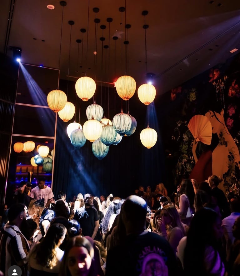 Crowded nightclub with illuminated hanging lanterns, blue stage lighting, and silhouetted attendees dancing and enjoying the event