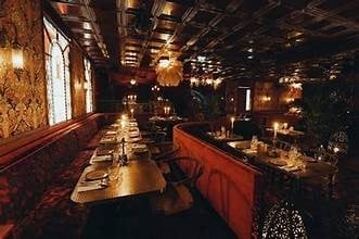 Upscale restaurant interior with long wooden tables, ambient warm lighting, exposed ceiling, and elegant table settings along both sides
