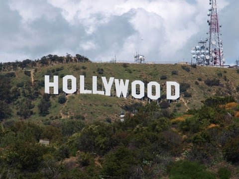 The Hollywood sign on a hillside covered in green vegetation with broadcast towers visible in the background