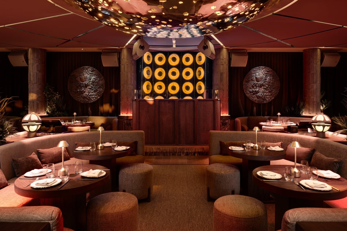 Upscale restaurant dining room with round tables, warm amber lighting, decorative spheres, and illuminated golden circular wall display