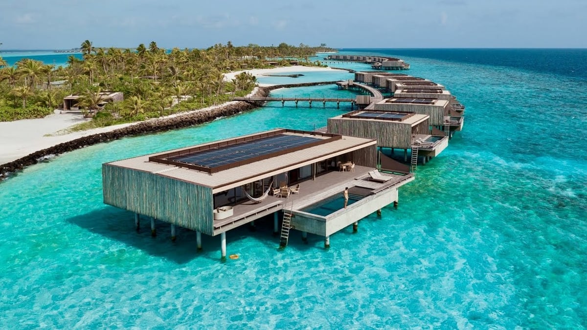 Overwater bungalows and docks in turquoise lagoon with tropical island and palm trees in background