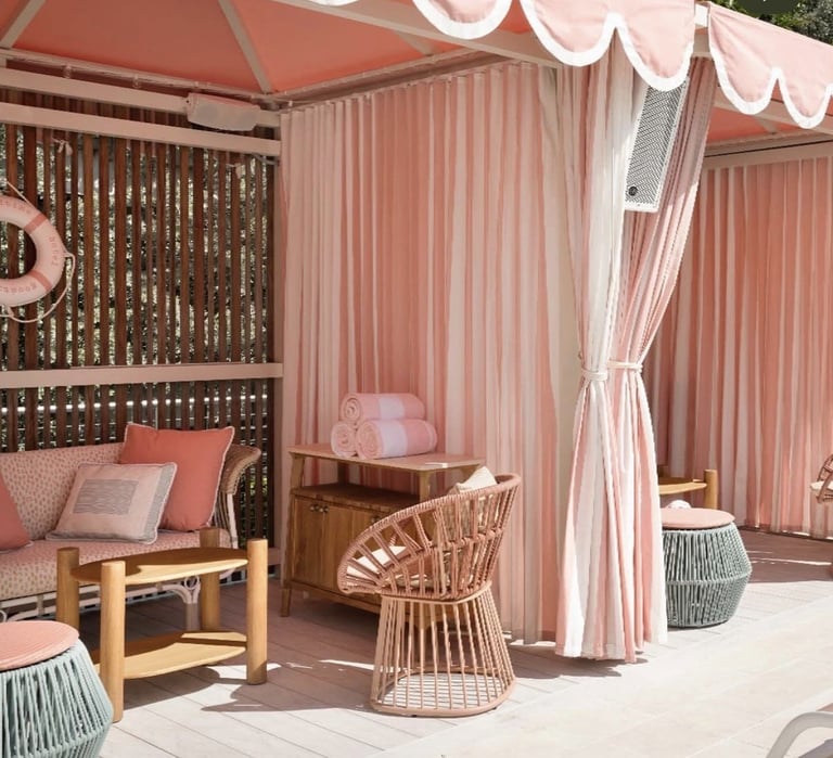 Stylish outdoor patio lounge with pink and white striped curtains, wooden furniture, wicker seating, and decorative pillows