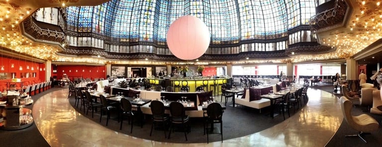 Modern luxury hotel lobby with circular bar seating, decorative pink sphere, arched ceiling with skylight, and elegant red and gold interior design