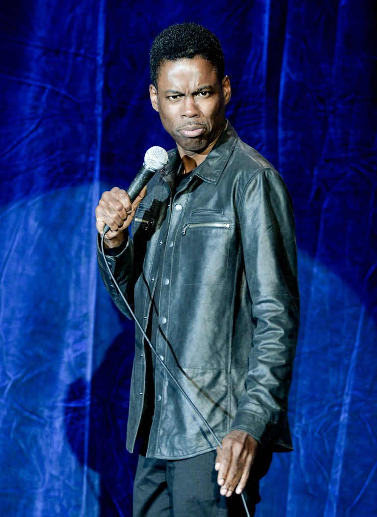 Man holding microphone on stage wearing dark leather jacket against blue textured backdrop