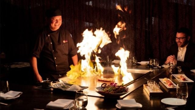 Chef performing tableside flambé with dramatic flames while diners watch at an upscale restaurant