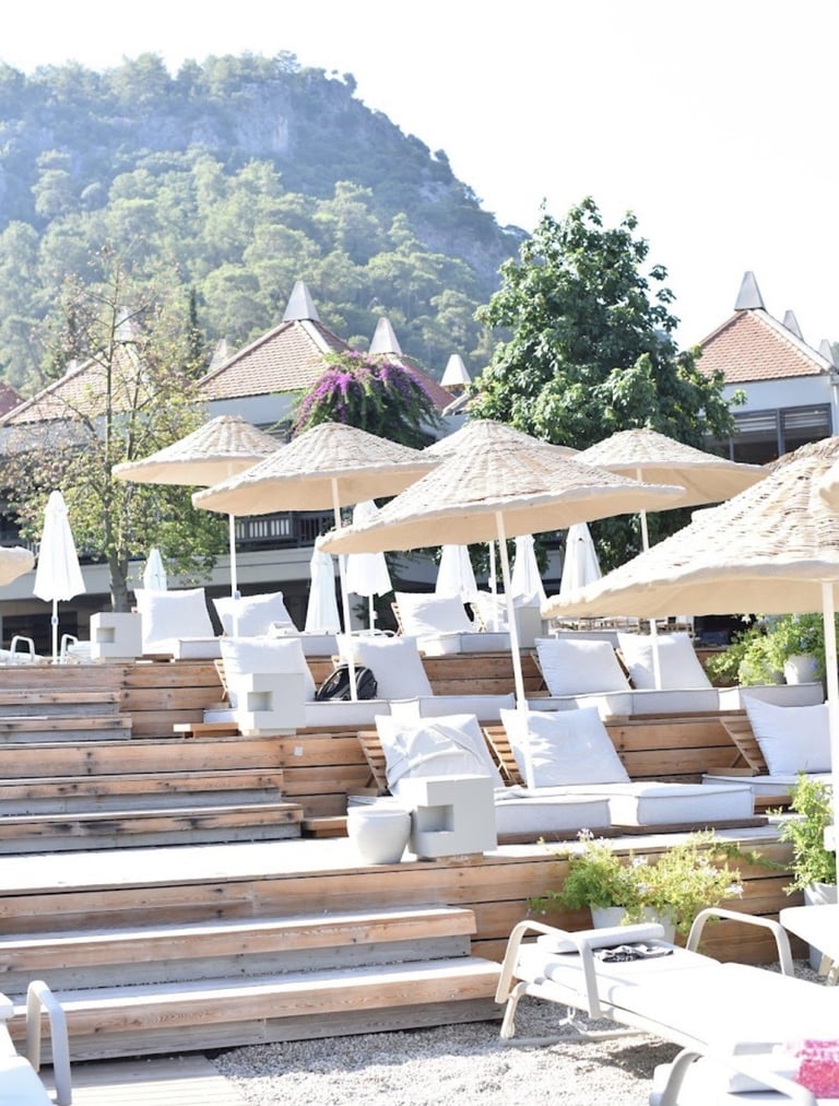 Luxury resort pool deck with wooden loungers, white cushions, tan umbrellas, and mountain views in background